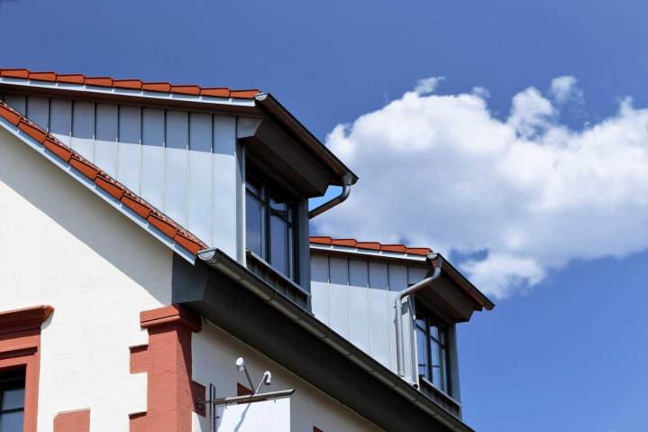 Ouvrier fixant des éléments de rive en zinc sur le bord dun toit, garantissant létanchéité latérale.