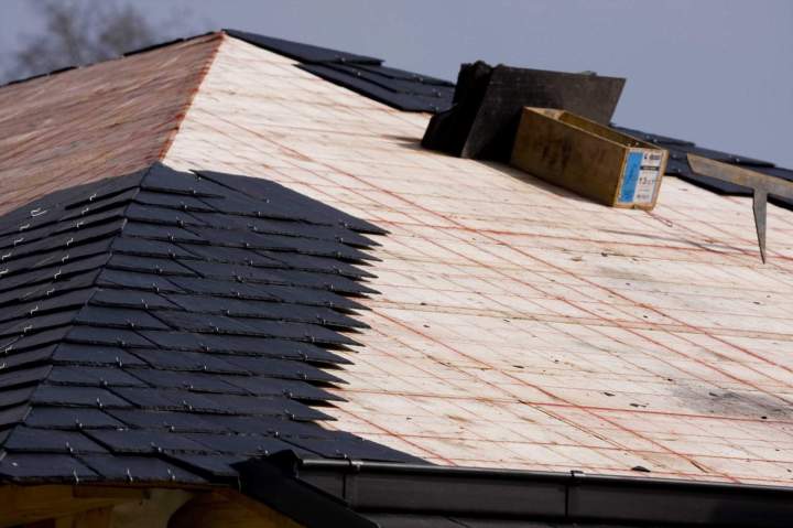 Vue de haut dune toiture ancienne en cours de rénovation, avec des ouvriers remplaçant des ardoises endommagées.